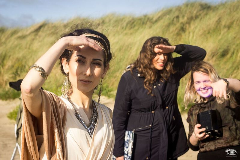 3 female figures stand looking forwards, shielding their eyes from the sun